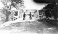 Two-Men-Standing-At-Metal-Bridge-On-Country-Road.jpg